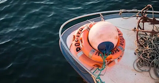 Boat deck with lifebuoys and ropes on water.