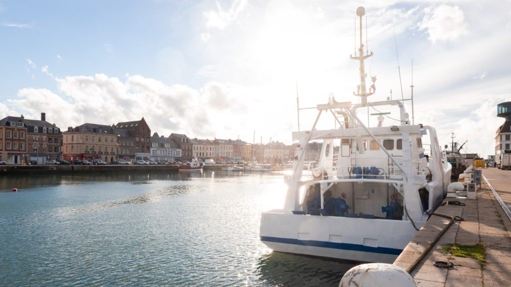Boat docked at a sunny harbor with buildings in the background.