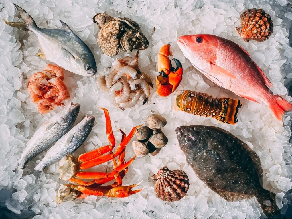 Assorted seafood on ice, including fish, shrimp, crab legs, clams, and shells.