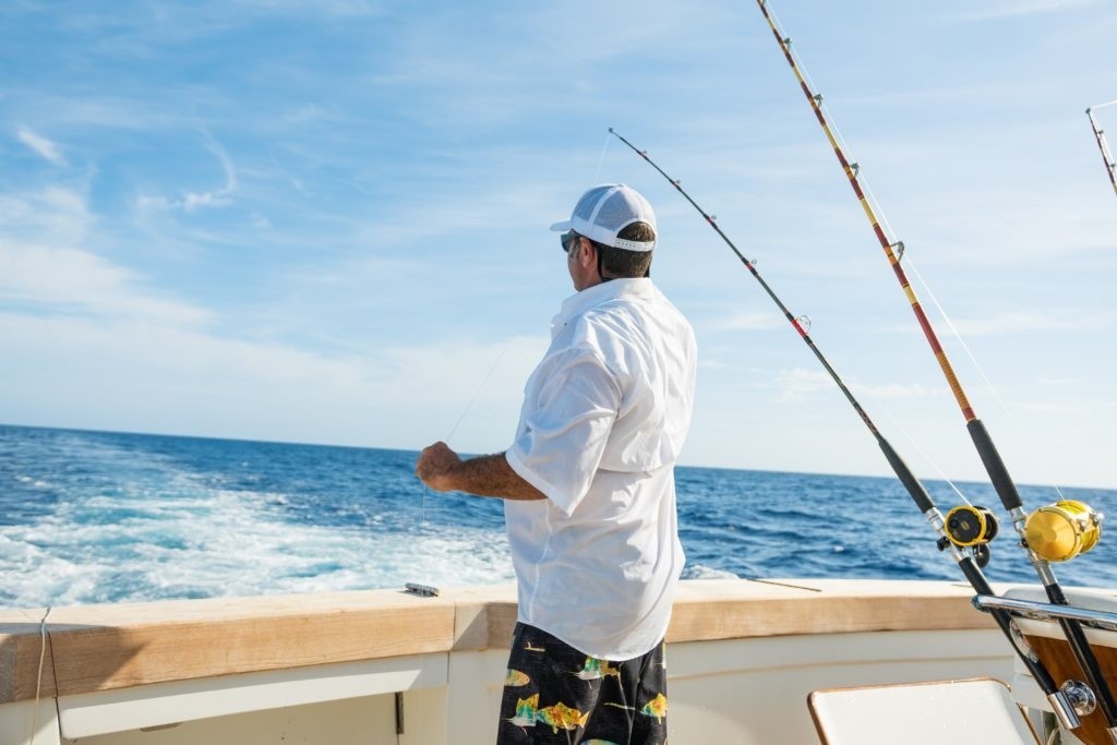 Man fishing on a boat in the ocean under a clear sky.